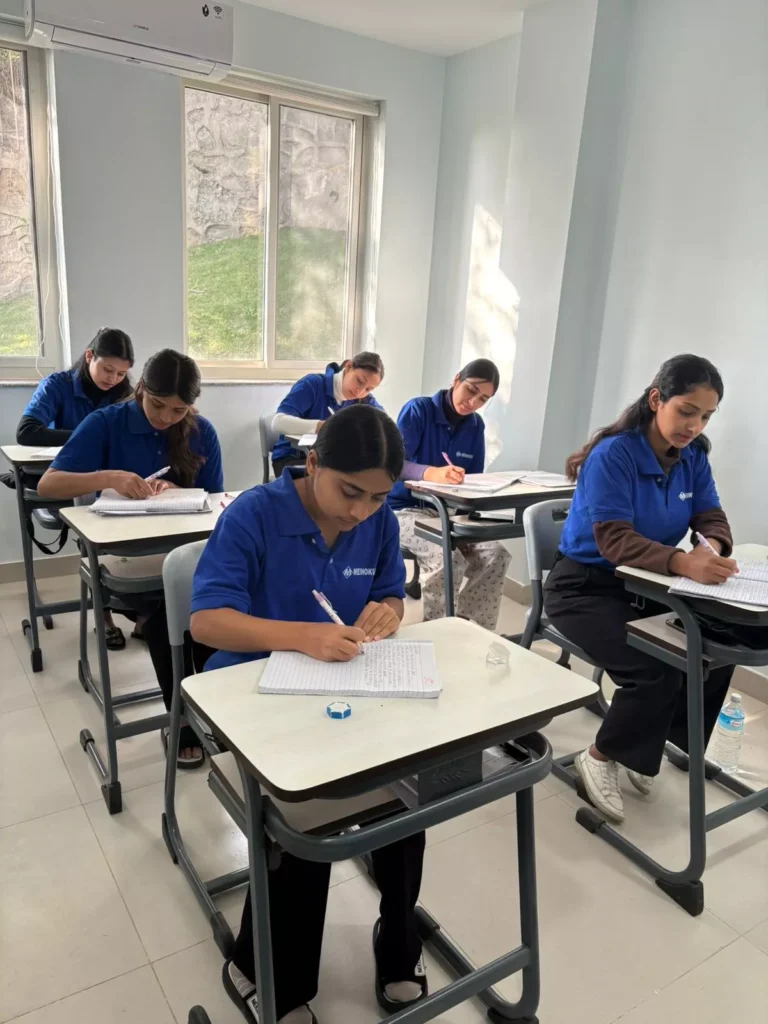 A group of students in blue uniforms takes a test in a bright classroom. They are focused on writing, conveying a mood of concentration and diligence.